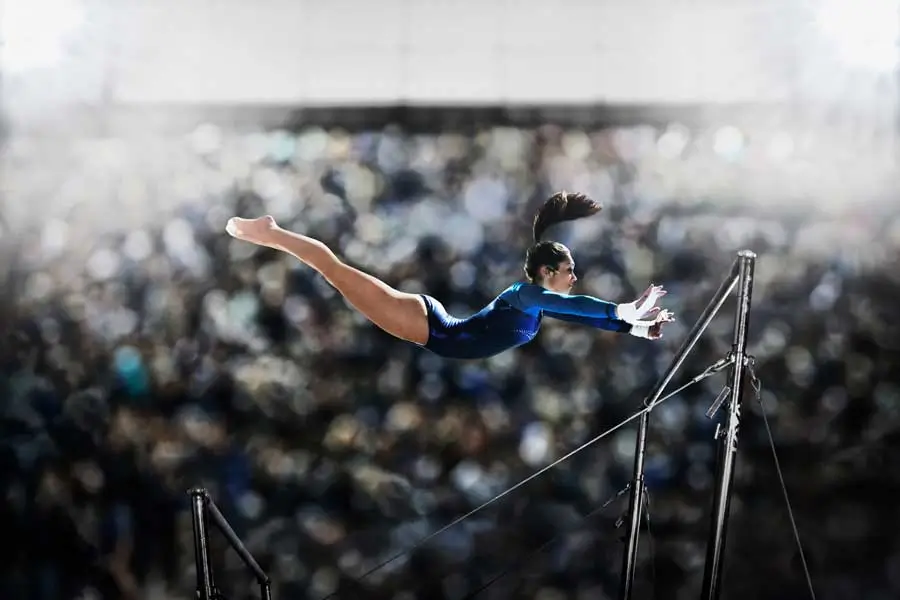 Female gymnast in mid-air reaching for the parallel bars